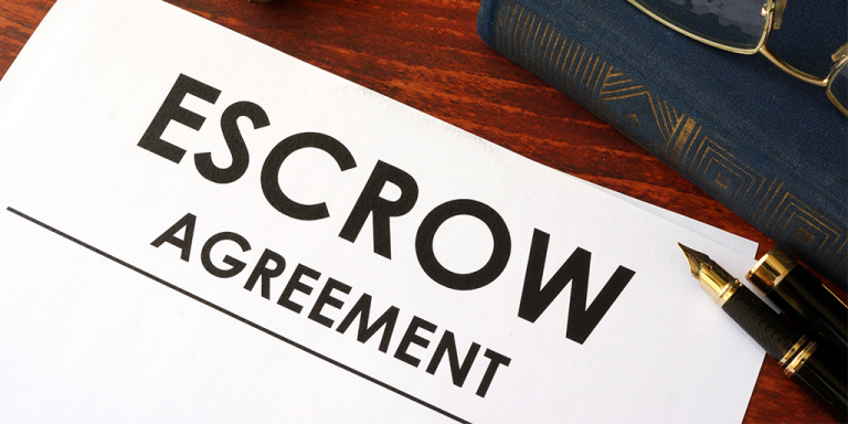 Paper with the words escrow agreement on a table with a pen and a book next to it