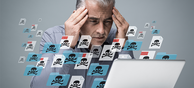 Frustrated Man massages his head in frustration as his laptop is taken over by Malware. Floating files surround him with skull and bones symbols.