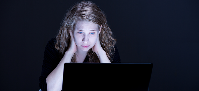 Girl looks sad and scared at computer, victim of cyberstalking, scared of cyberstalkers.