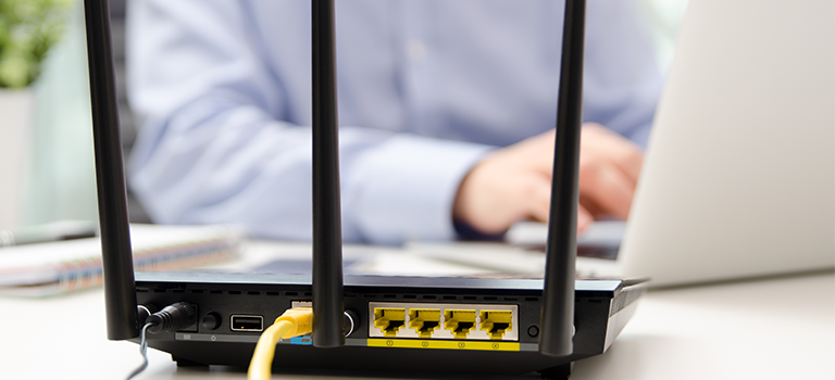 Firewall Hardware and Firewall Software appearing as a cage in front of a blurred out man typing on his computer.