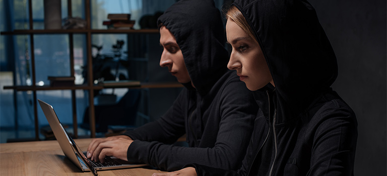 Cybersecurity Culture. Side View Of Hackers In Black Hoodies Using Laptops At Wooden Tabletop, Cyber Security Concept